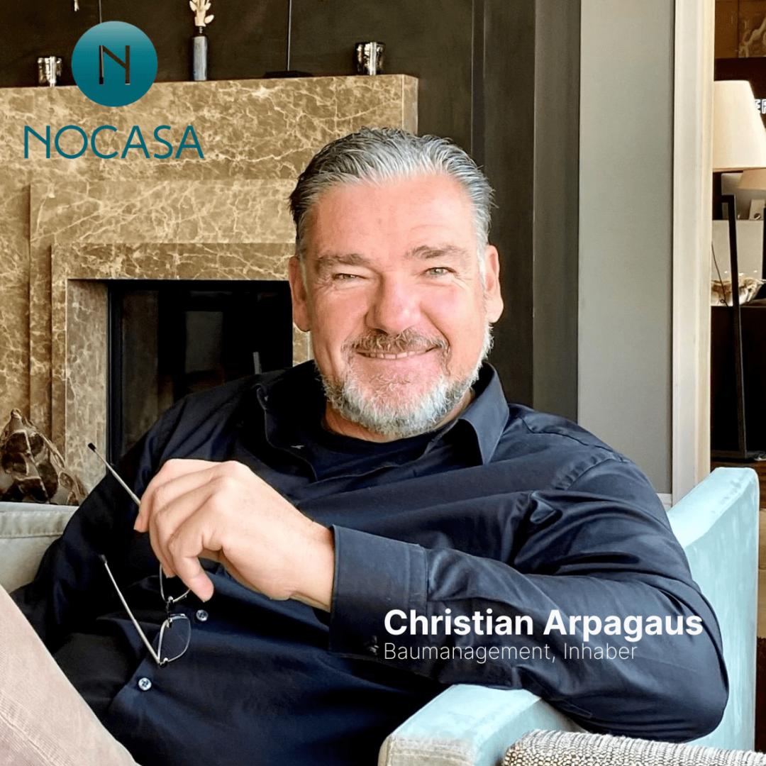 Christian Arpagaus von Nocasa. Ein Mann sitzt auf dem Sofa mit Brille in der Hand und lächelt freundlich